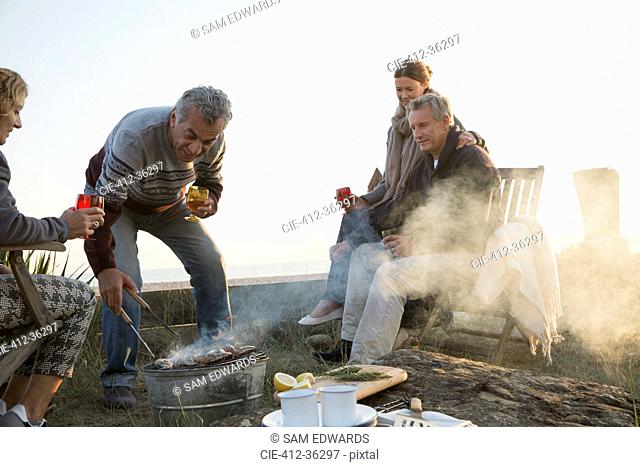 Mature couples barbecuing and drinking wine on sunset beach