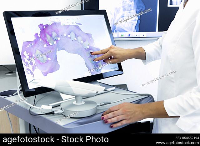 Unrecognizable doctor browsing 3D scan of patient teeth on computer monitor while working in contemporary clinic