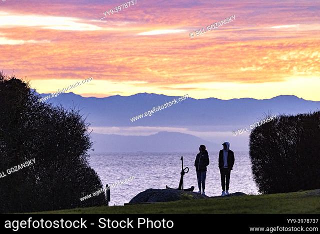 Couple watching the sunset over the Salish Sea from Saxe Point Park in Esquimalt - Victoria, Vancouver Island, British Columbia, Canada