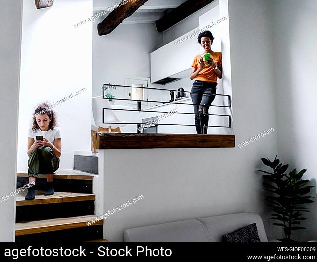 Two young women using their smartphones at home