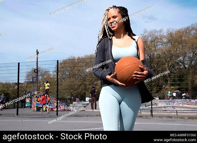 Smiling woman holding basketball walking in sports court