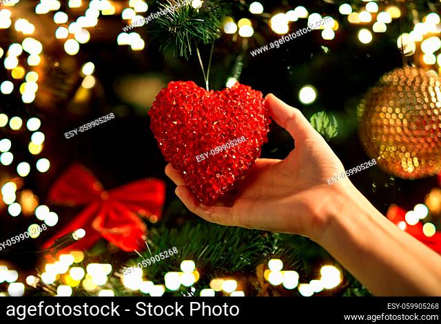 hands decorating christmas tree with red heart