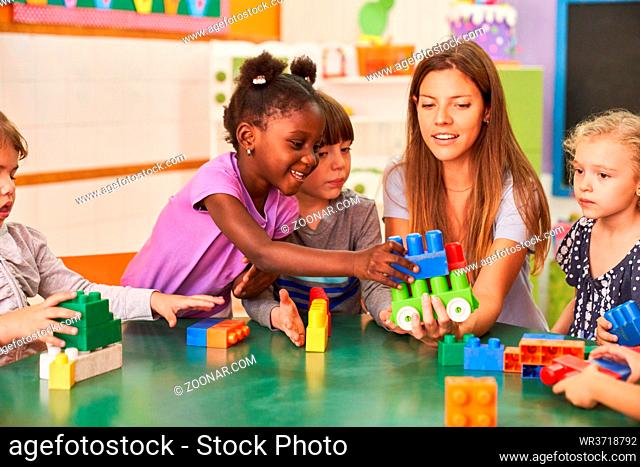 Kinder spielen zusammen mit Bausteinen im internationalen Kindergarten mit Kindergärtnerin