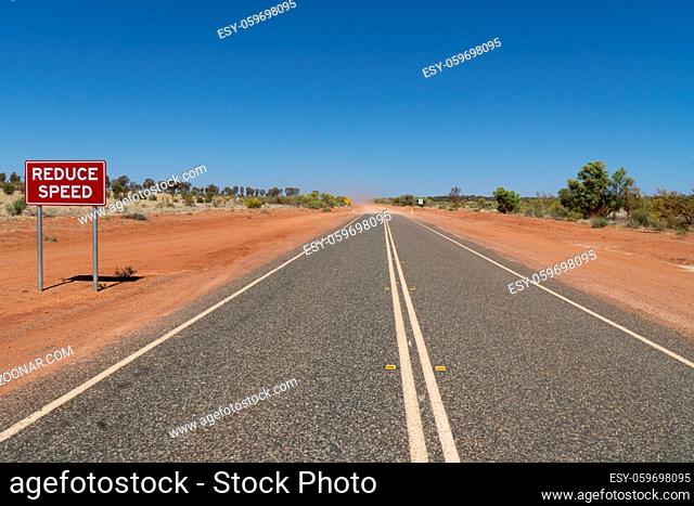 on a highway in the Australian outback there is a red sign with the inscription Reduce Speed