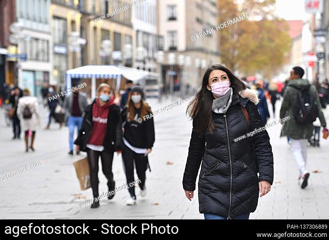 Mask compulsory in the pedestrian zones and public places in Munich on 11.11.2020. Young woman with everyday mask telephones with smartphone