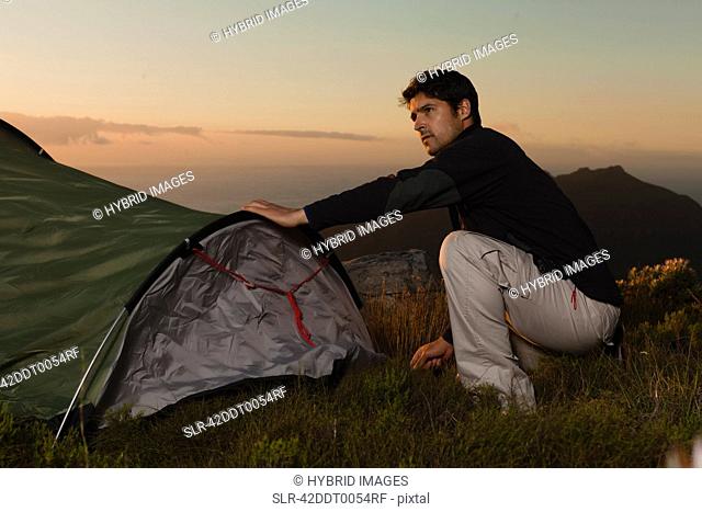 Hiker setting up tent on hillside