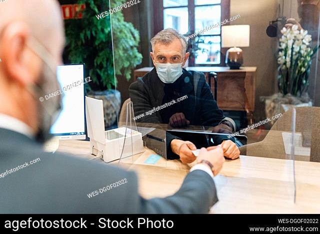Mature man taking cardkey from receptionist at hotel reception