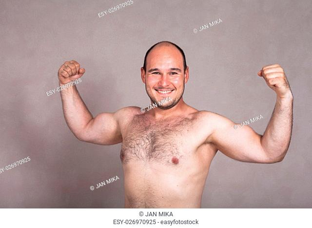 Portrait of happy shirtless man posing and showing his strong arms and hairy body