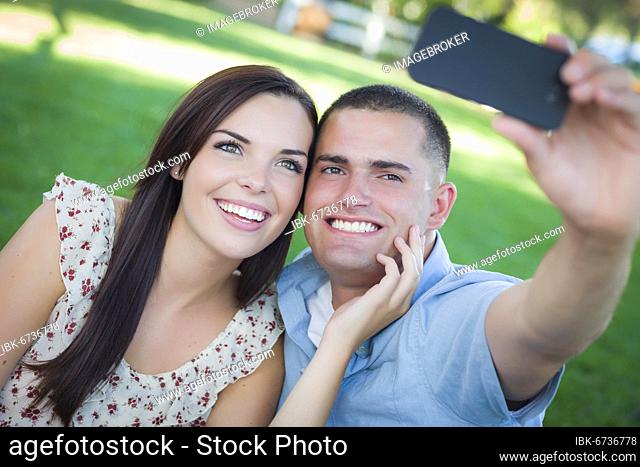 Happy mixed-race couple taking self portrait with A smart phone in the park