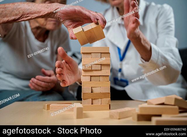 Senior woman practice skills, build wooden blocks, build tower and try not to let it fall, Jenga game. Old patient pull out block, place on top