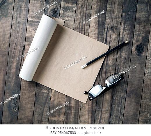 Blank notebook of kraft paper, glasses and pencil on wood background. Flat lay