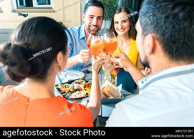 Four friends holding stemmed wine glasses while toasting together with a cold refreshing alcoholic drink during a delicious lunch at the restaurant