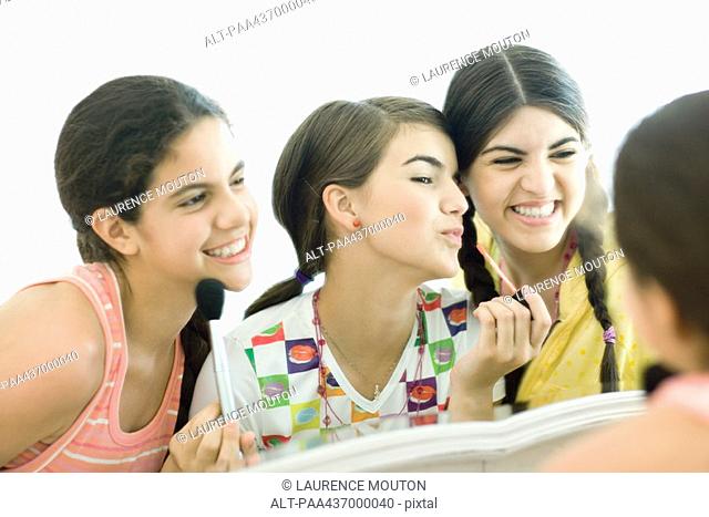 Three young female friends putting on make-up
