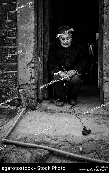 Street scene in an old town quarter of Chongqing. Old woman in her front door, these neighbourhoods are gradually being demolished to make room for new...