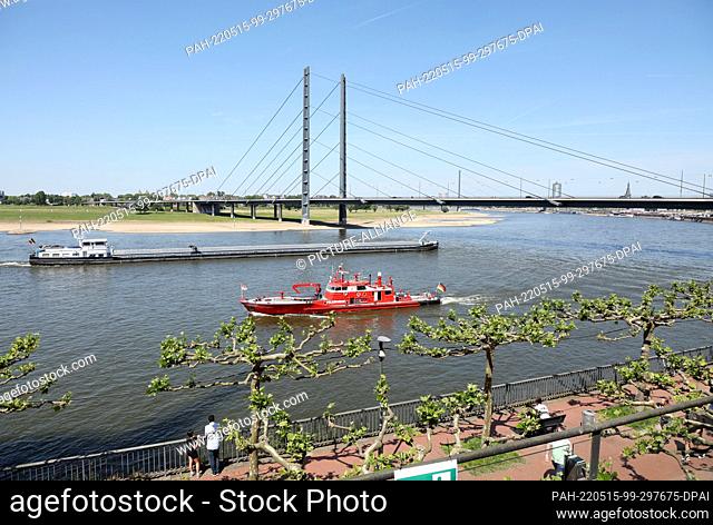 15 May 2022, North Rhine-Westphalia, Duesseldorf: A cargo ship and a fire boat are sailing on the Rhine in front of the Rhine knee bridge