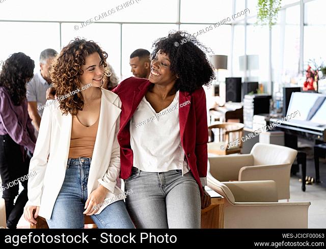 Happy businesswomen looking at each other sitting on table at office