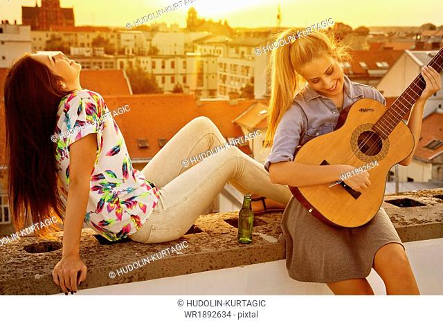 Young woman with girlfriend playing guitar at rooftop party