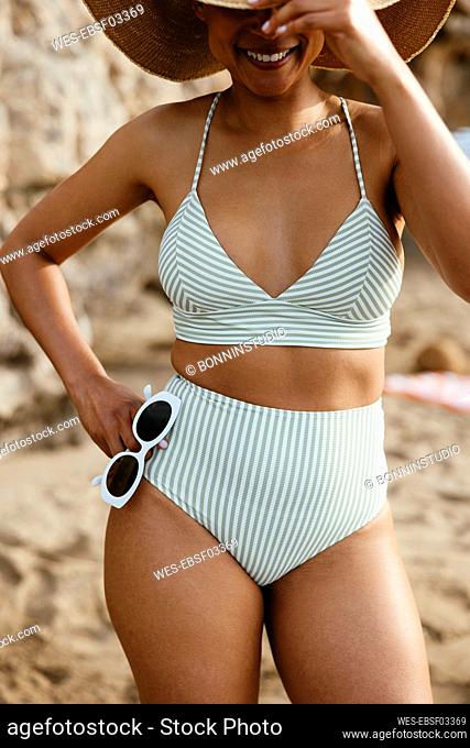 Woman in bikini standing with sunglasses at beach