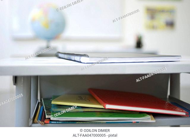 School desk containing stack of books, notebooks
