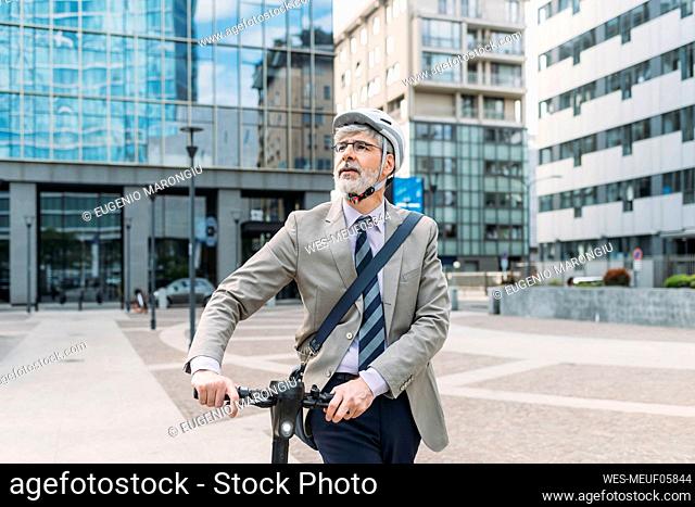 Businessman walking with electric push scooter in front of modern office buildings