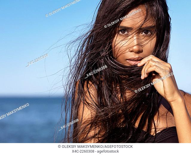 Expressive portrait of a beautiful young woman with long wet dark hair blown in the wind with sea in the background