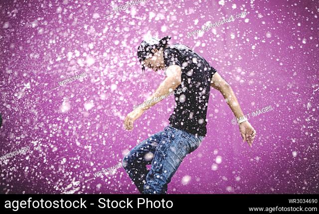 Young man standing in a shower of water drops