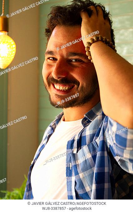 young man posing with natural light from window with carefree pose smiling