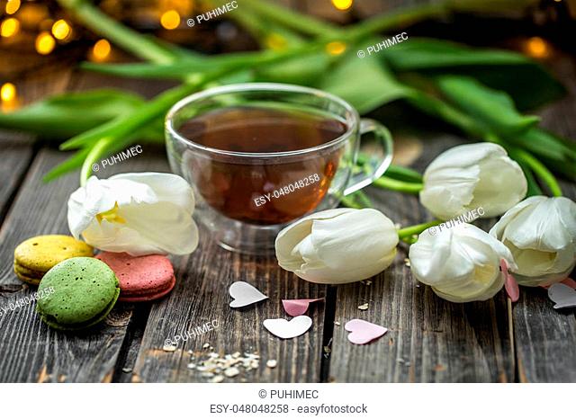 beautiful white tulips and a transparent Cup of tea with a macaron on wooden background, holiday concept