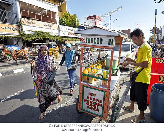 Muslim women walk by street vendor selling fresh fruit juices on Malioboro Street. Yogyakarta, Java, Indonesia