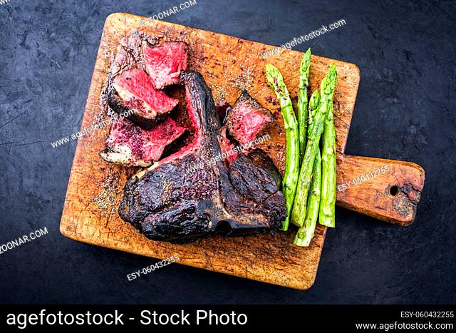Barbecue dry aged wagyu bistecca alla fiorentina beef steak sliced with large filet piece with green asparagus and red wine salt offered as top view on an old...