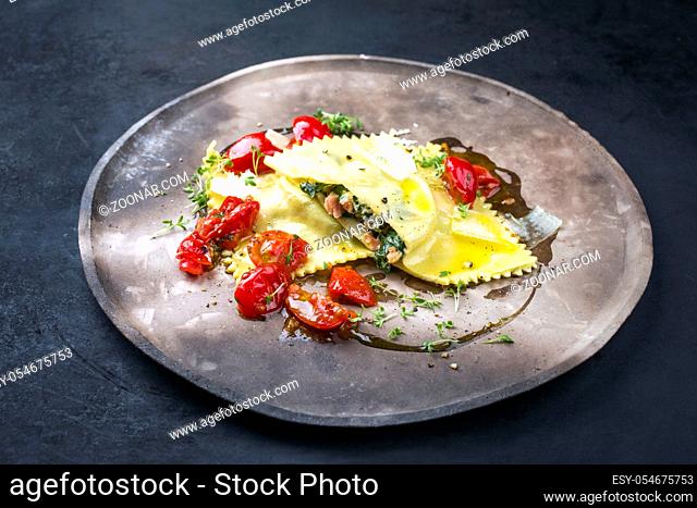 Traditional Italian ravioli pasta offered with salmon spinach filling and fried tomatoes as closeup on a modern design plate