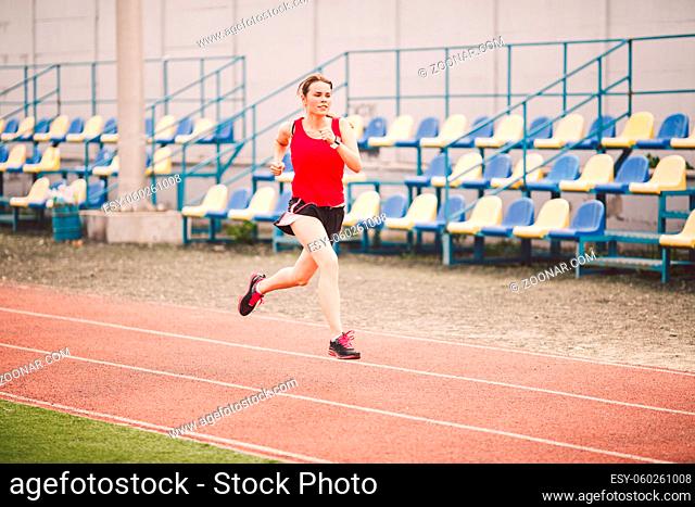 Female runner jogging on stadium track, woman athlete running and working out outdoors, sport and fitness concept. Young woman in sportswear training on a...