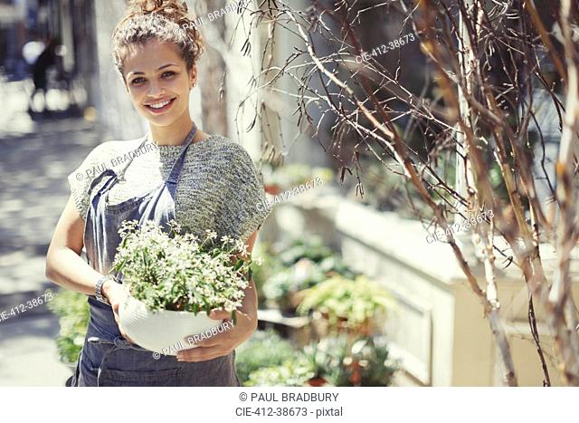 Portrait smiling female florist holding potted plant at sunny storefront
