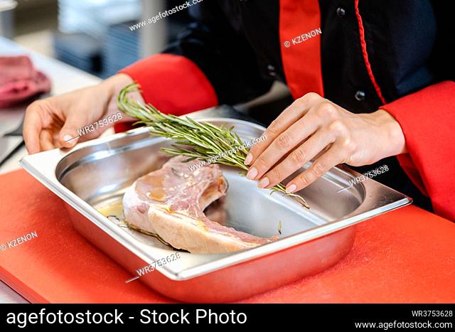 Close up shot of a female chef putting rosemary seasoning on a lamb steak