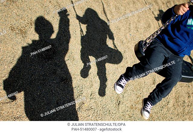 The shadow of a man and a refugee boy are cast onto the sand on a playground in the state accomodation office in Brunswick, Germany, 27 August 2014