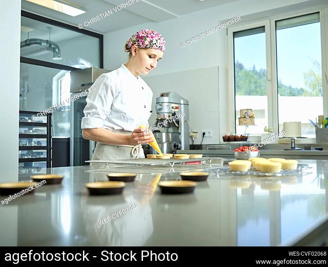 Young confectioner decorating cupcakes with icing in kitchen