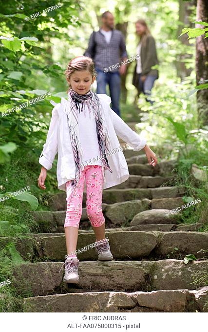 Girl walking down stone steps in woods, parents in background