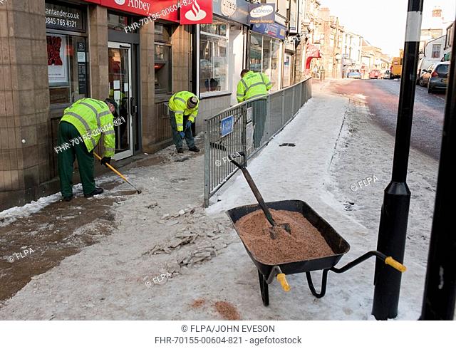 Council workers clearing ice and gritting pavement in town, Clitheroe, Lancashire, England, winter