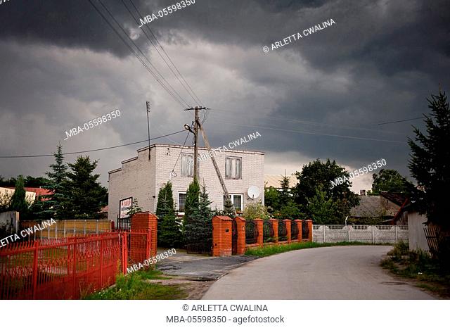 Gloomy stormy weather above brick house with antenna on roof in Odrzywol, Poland, Europe, Building, red bricks gate and fence