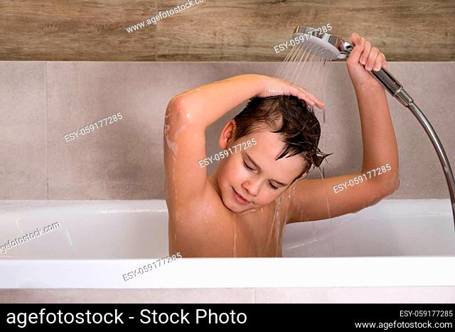 The boy holding shower head and washes his head in bathroom Happy healthy childhood