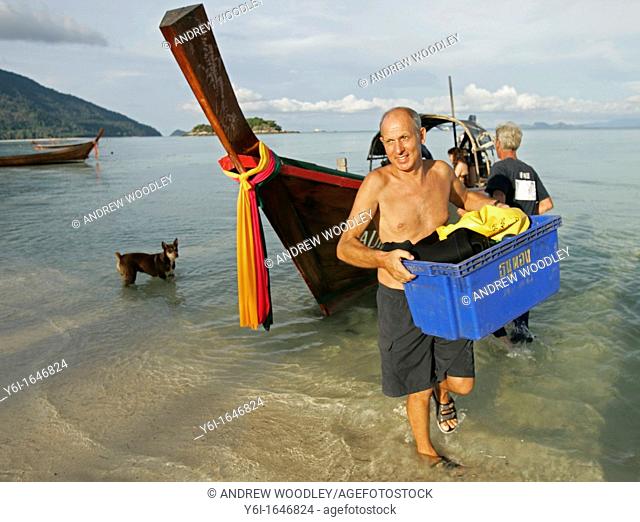 Man carries ashore diving equipment from traditional longtail boat Ko Lipe island Thailand
