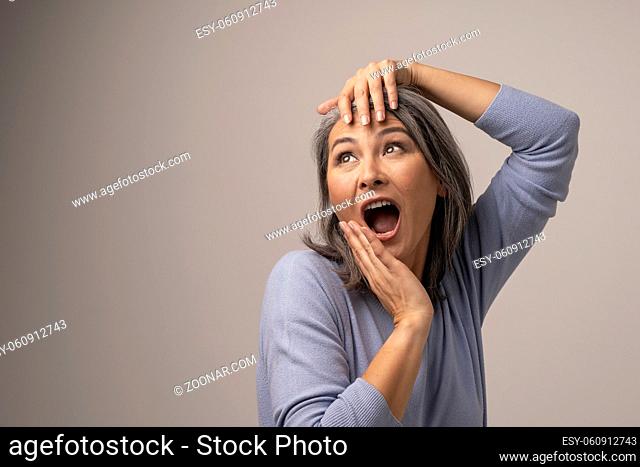 Expressive Woman Poses And Screams Out Loud. Beautiful Middle-Aged Woman Widely Opens Her Mouth And Touches Her Head Posing For The Camera. Portrait