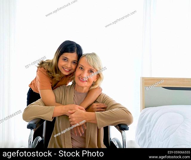 Happy mix skin family living together, adopted asian daughter cuddle caucasian mother sitting on a wheelchair with smiles