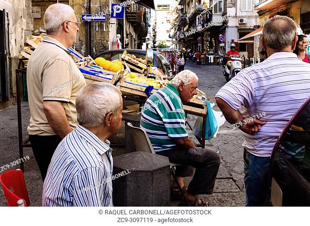 Group of old man killing time while talking sit next to fruits street stall, Naples, Campania, Italy