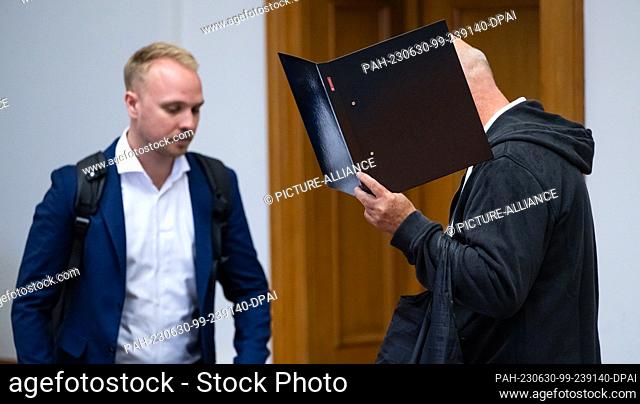 30 June 2023, Lower Saxony, Lüneburg: The defendant (r) enters the hearing room in the regional court and covers his face with a file folder