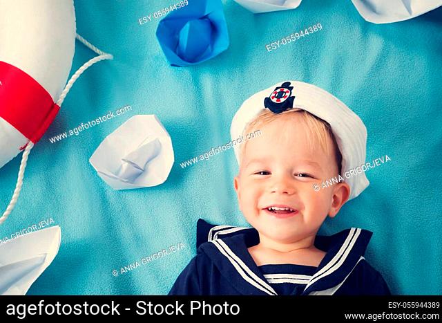 two years old boy playing in sailor hat. Child with paper ships on blue background