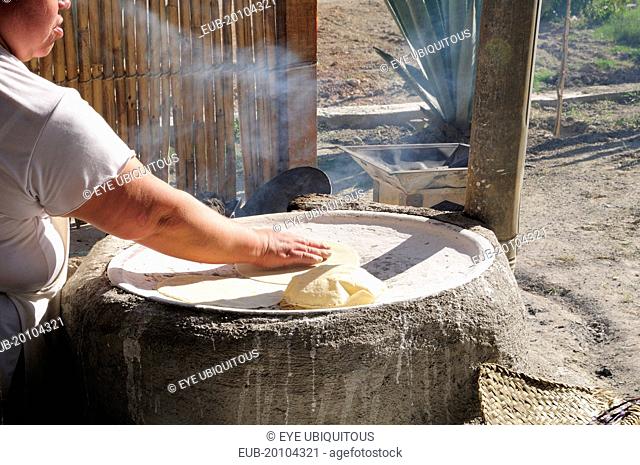 Woman making tortillas outside on traditional comal griddle