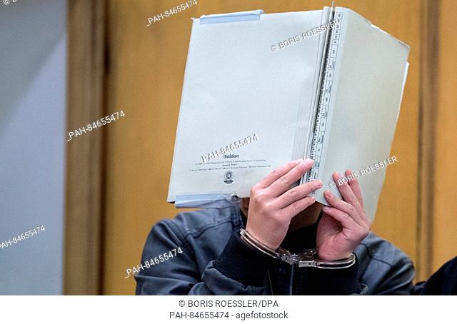 A defendant arrives in a courtroom while covering their face with a folder in Frankfurt am Main, Germany, 10 October 2016