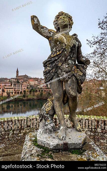 A statue of a goddess on a terrace overlooking the river Tarn to the city skyline of Albi