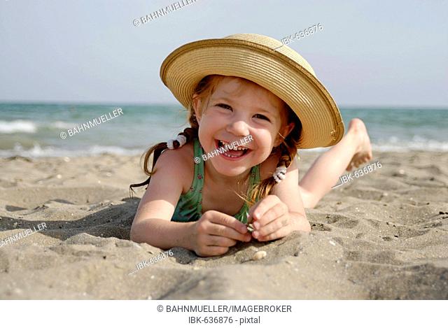 Little girl lies at a sandy beach at the sea